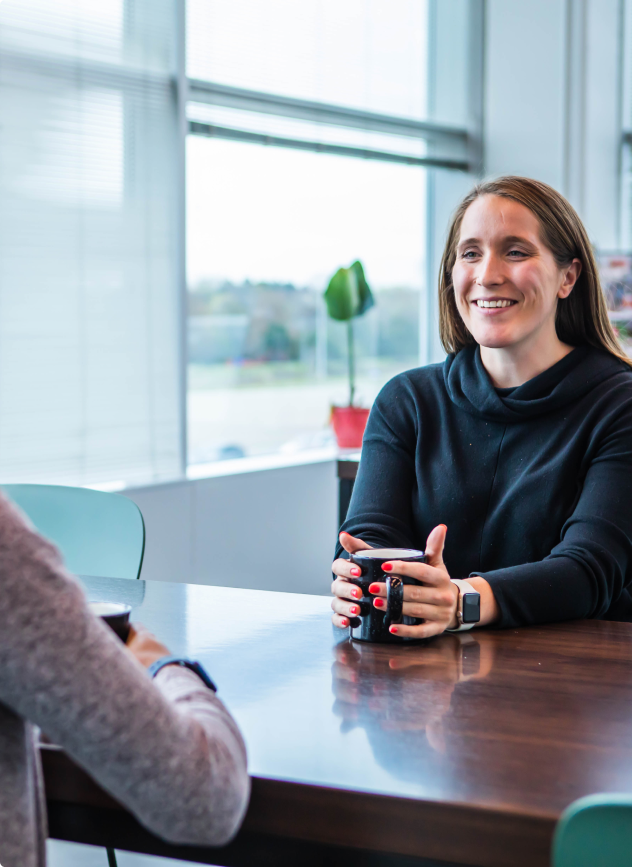 woman sitting at a desk holding a cup and smiling